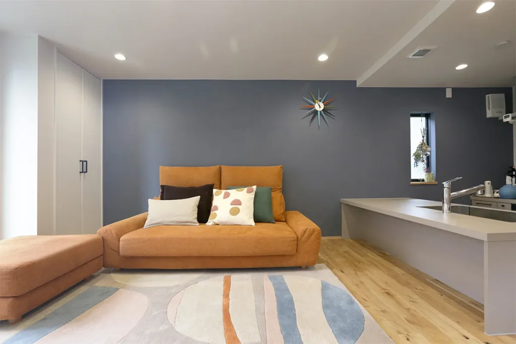 リビングの一面をネイビーにして大胆にメリハリを。ソファのオレンジとのコントラストがおしゃれ。